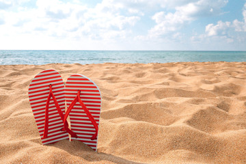 Red slippers in yellow sand on a beach near the sea, summer vacation
