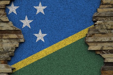 Solomon Islands flag depicted in paint colors on old stone wall closeup. Textured banner on rock...