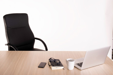 An empty black armchair at a wooden desk with a open laptop, cup of tea, notebook, reading glasses and mobile phone. Negative space. Copy space area for advertising.