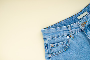 Light blue mom denim jeans with pocket at ivory color pastel background. Modern fashion flat lay.
