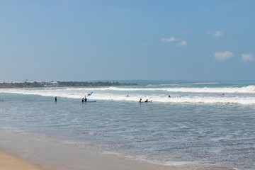 KUTA / INDONESIA - OCTOBER 25, 2019: Sandy beach with waves and surfers at noon.