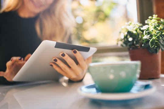 A young woman drinking a beverage from a cup and using her tablet in the morning.
