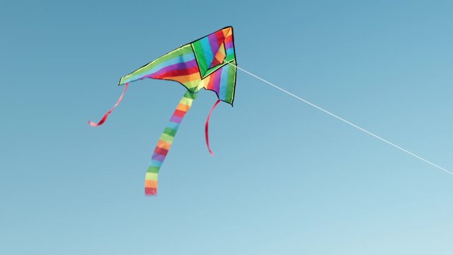 Colored kite with an emoji hangs in the air against a blue sky on a sunny summer day at a city kite festival. The tail of a kite sways in the wind. Children's 