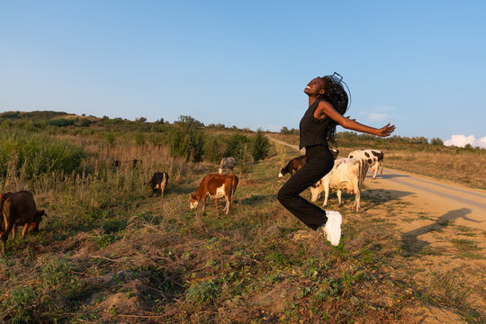 Young happy smiling african girl jumps among the field, cows grazed on the background
