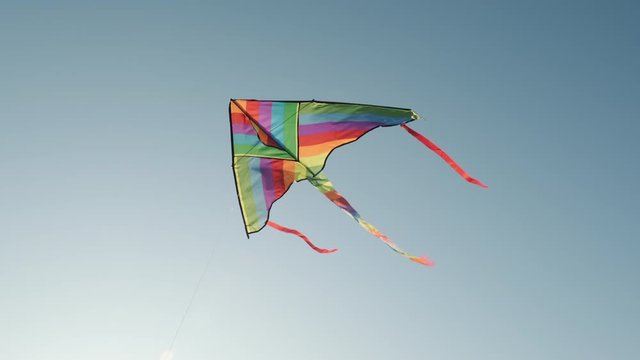 Colored kite with an emoji hangs in the air against a blue sky on a sunny summer day at a city kite festival. The tail of a kite sways in the wind. Children's 