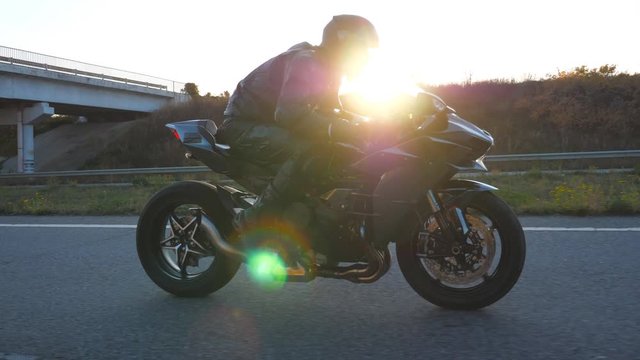 Man riding on modern sport motorbike at highway with sun flare at background. Motorcyclist racing his motorcycle on country road. Guy driving bike during trip. Concept of freedom. Slow motion