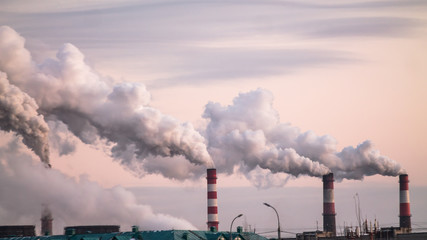 industrial chimneys with heavy smoke causing air pollution as ecological problem on the pink sunset...