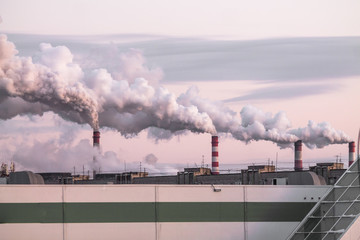 industrial chimneys with heavy smoke causing air pollution as ecological problem on the pink sunset...