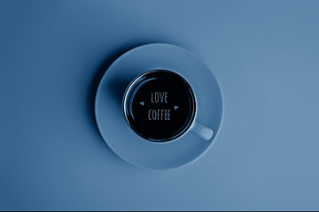 Cup of espresso coffee with text love coffee on a saucer in blue tones. Flatlay. View from above.