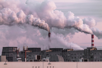 industrial chimneys with heavy smoke causing air pollution as ecological problem on the pink sunset sky background