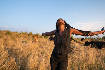 Happy young african girl in black clothes dance among the dry grass field, cows graze on the...