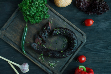 The blood sausage on a dark cutting board is decorated with fresh herbs and vegetables. Blood...