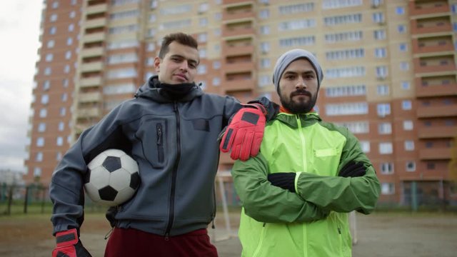 Waist up arc shot of confident middle eastern soccer player and goalkeeper standing together on outdoor sports field and looking at camera