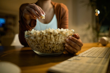 Close-up of woman eating popcorn in the evening at home.