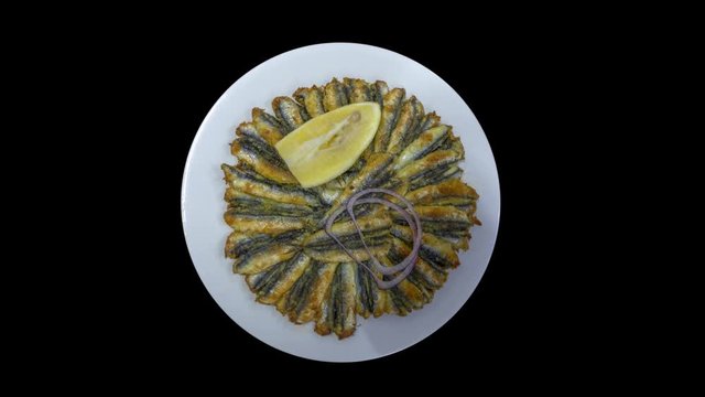 Turkish fried anchovy (hamsi tava), lemons and onion are served with white plate in black