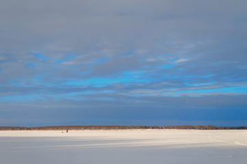 Fototapeta na wymiar A lonely small man walks under a turquoise sky through a snowy field. The horizon between the sky and the snow field divides the frame in a ratio of one to four. You can place text on top.