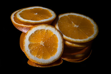 Fresh organic orange fruit, sliced, with reflection on shiny black background