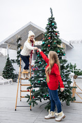 Mother and the daughter decorate a Christmas tree outdoors.