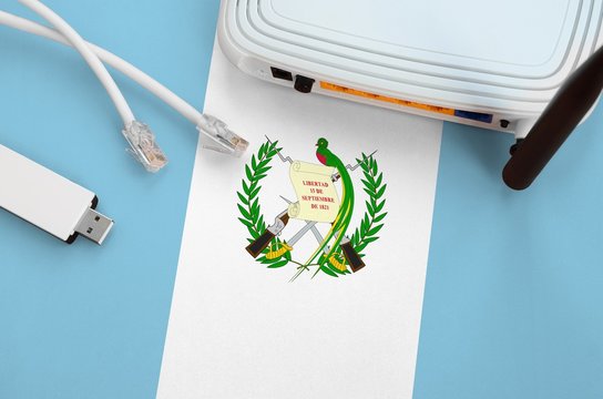Guatemala flag depicted on table with internet rj45 cable, wireless usb wifi adapter and router. Internet connection concept