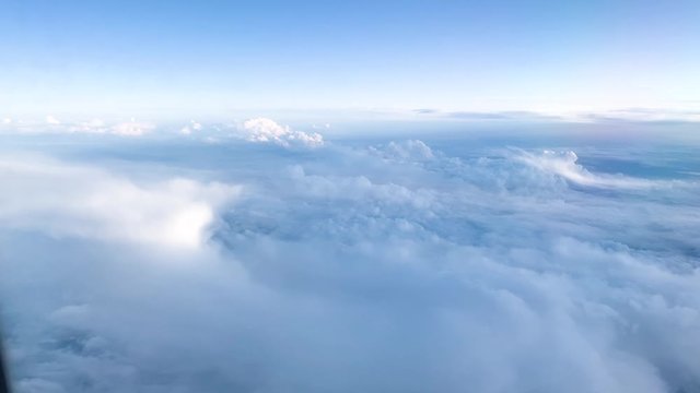 aerial view of white clouds and blue sky from airplane window in cabin