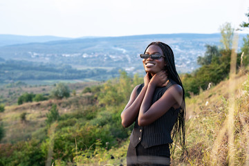 Naklejka premium Close up portrait of the young happy african girl in black clothes and sunglasses that smiling and looking at the camera