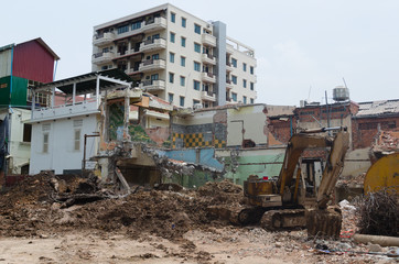 Fototapeta na wymiar Demolished old house. Excavator crashed at demolition construction site near damaged building. New residential building on background. Phnom Penh, Cambodia.