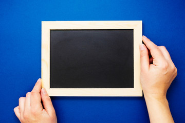 Chalkboard mock up. Female hands holding blackboard on a blue background, isolated. Copy space, flat lay. Business, education concept.