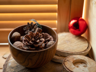 Wooden Cup with a cone and walnuts on the windowsill. Wooden blinds. Red Christmas ball.
