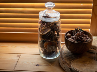 Wooden Cup and glass with a cone and walnuts on the windowsill. Wooden blinds.