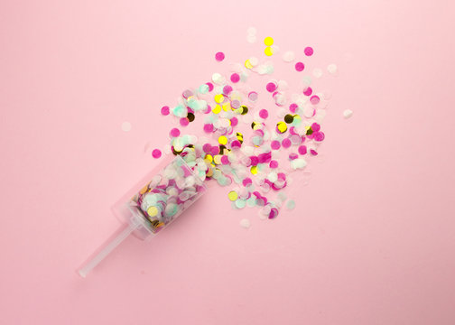 Popper with multi-colored paper confetti on a pink background.