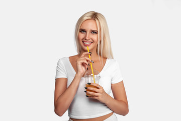 Funny cute attractive careless blonde woman is drinking cocktail in a plastic cup using a straw, isolated on white background. So delicious. Sexy smiling girl with juice.