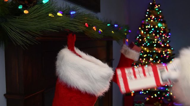 A close-up of Santa Claus&rsquo;s hand placing a pair of blank ticket stubs into a Christmas Stocking hanging on a mantelpiece with a Christmas tree with twinkling lights in the background
