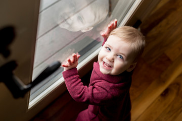 Happy, cozy baby looking up with reflection in glass door
