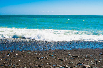 Blue oncoming wave of surf on a rocky pebble beach. Sunny day.