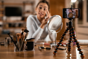 Close-up of woman vlogging while applying eyeshadow at home.