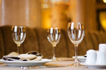 wineglasses, plates and napkins served on a table ready for a dinner party in a rich restaurant, shallow depth of field, blurred background