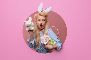 Happy Easter. Young woman with bunny ears and basket full of Easter eggs on pink background. crawls...