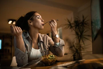 Fotobehang Below view of woman with eyes closed enjoying in a taste of healthy salad. © Drazen