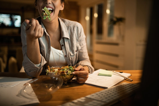 Hungry woman eating salad while working late on a computer.