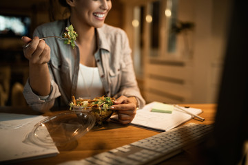 Freelancer worker eating salad while using desktop PC at night.