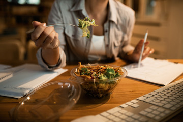 Close-up of woman eating salad while working late at home.