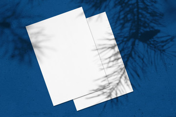 Empty white vertical rectangle poster mockups lying on each other with soft pine branch shadow on...