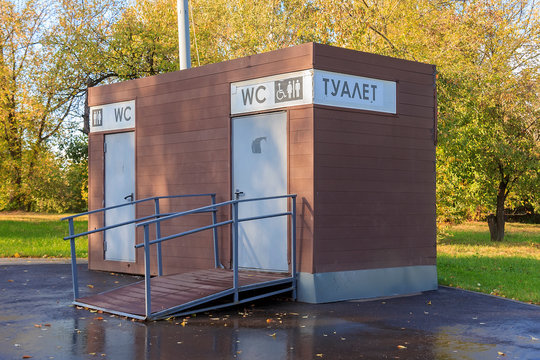 Public toilet in the autumn park. Text in Russian: toilet. WC. Free paying public WC. WC public toilet to man, woman and disabled in a park 