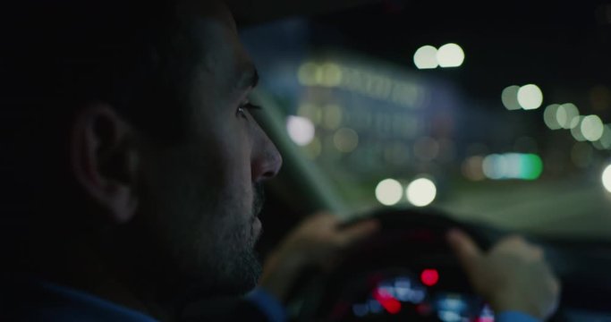 Slow motion close up of an young handsome businessman driving a modern car in center of the city by night. Shot in 8K. Concept of business, success, traveling, luxury