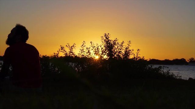 Silhueta de um homem no fim de tarde assistindo o p&ocirc;r do sol 