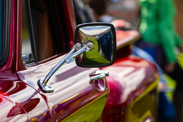 classic antique American red pickup car side chrome mirror close up view, people in the background during outdoor old cars show