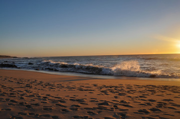 Obraz premium Orange sunset over the ocean. Waves in sunlight. Sandy beach which reflects the sunset. Winter sunset on beach