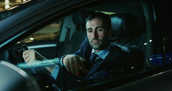 A handsome businessman is using an application of self pilot on a futuristic screen with augmented reality holograms  before a drive a car.