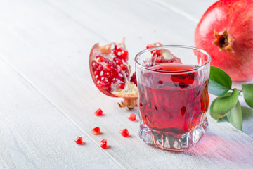 Glass of pomegranate juice and ripe pomegranate on a white wooden background. Healthy drink concept. Сopy space