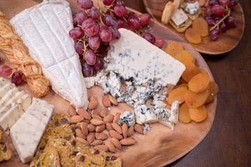 Wooden cheese platter with brie, assorted cheeses, red grapes, crackers and nuts